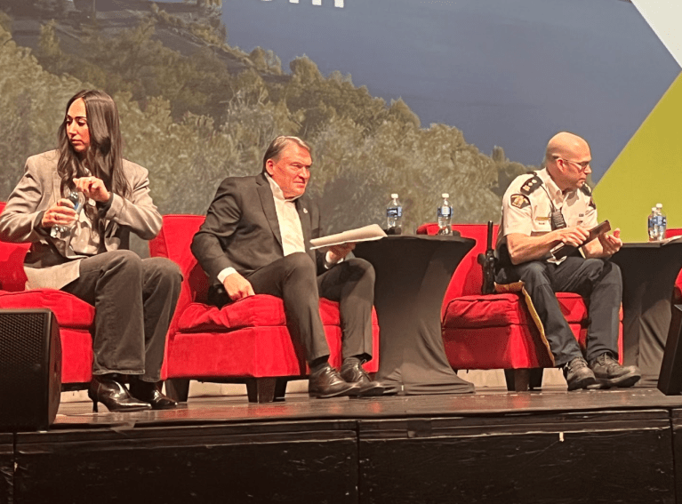Three people in red chairs on a stage.