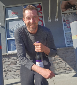 A man holds a bottle of wine outside a liquor store.