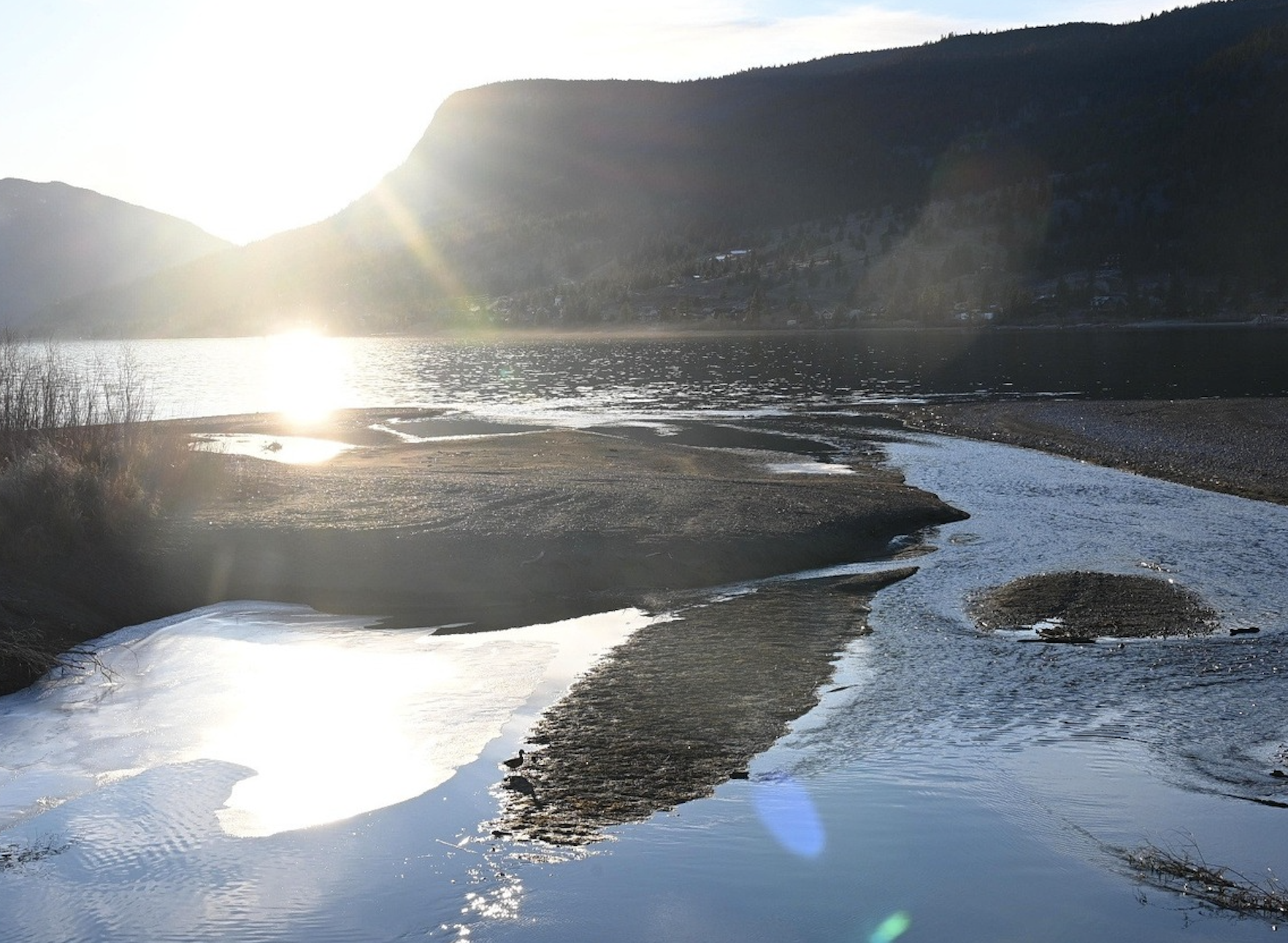 The sun poking out over some mountains and reflecting off the water.