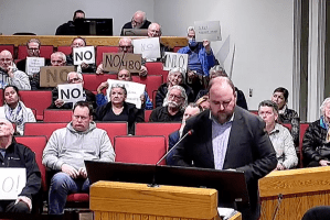 People holding signs that say "no" in council chambers.