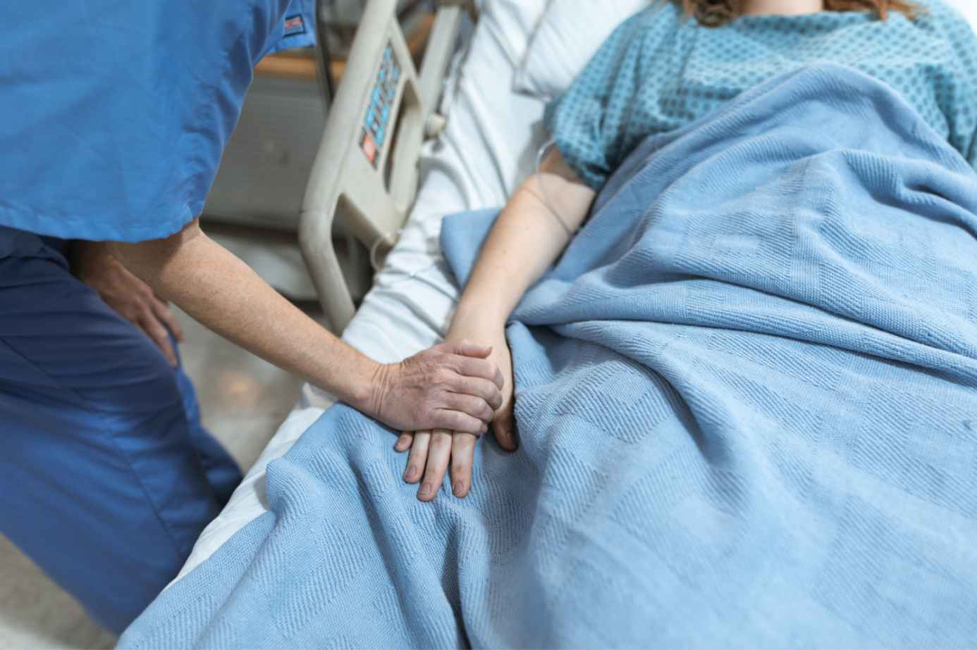 A nurse puts her hand on a patients hand in their bed.