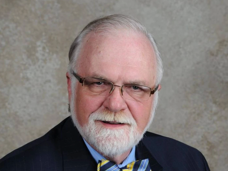 A man with white hair and a white beard wearing glasses poses for a photo.