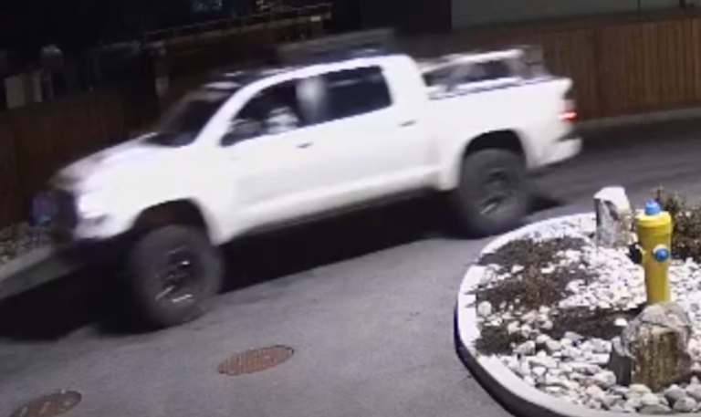 A blurry screen capture of a white, lifted pickup truck.
