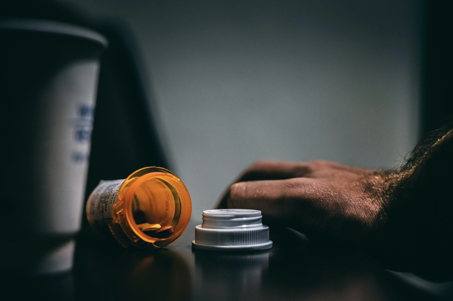 An orange pill bottle and a hand on a table