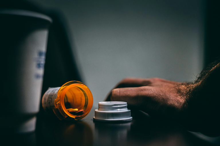 An orange pill bottle and a hand on a table