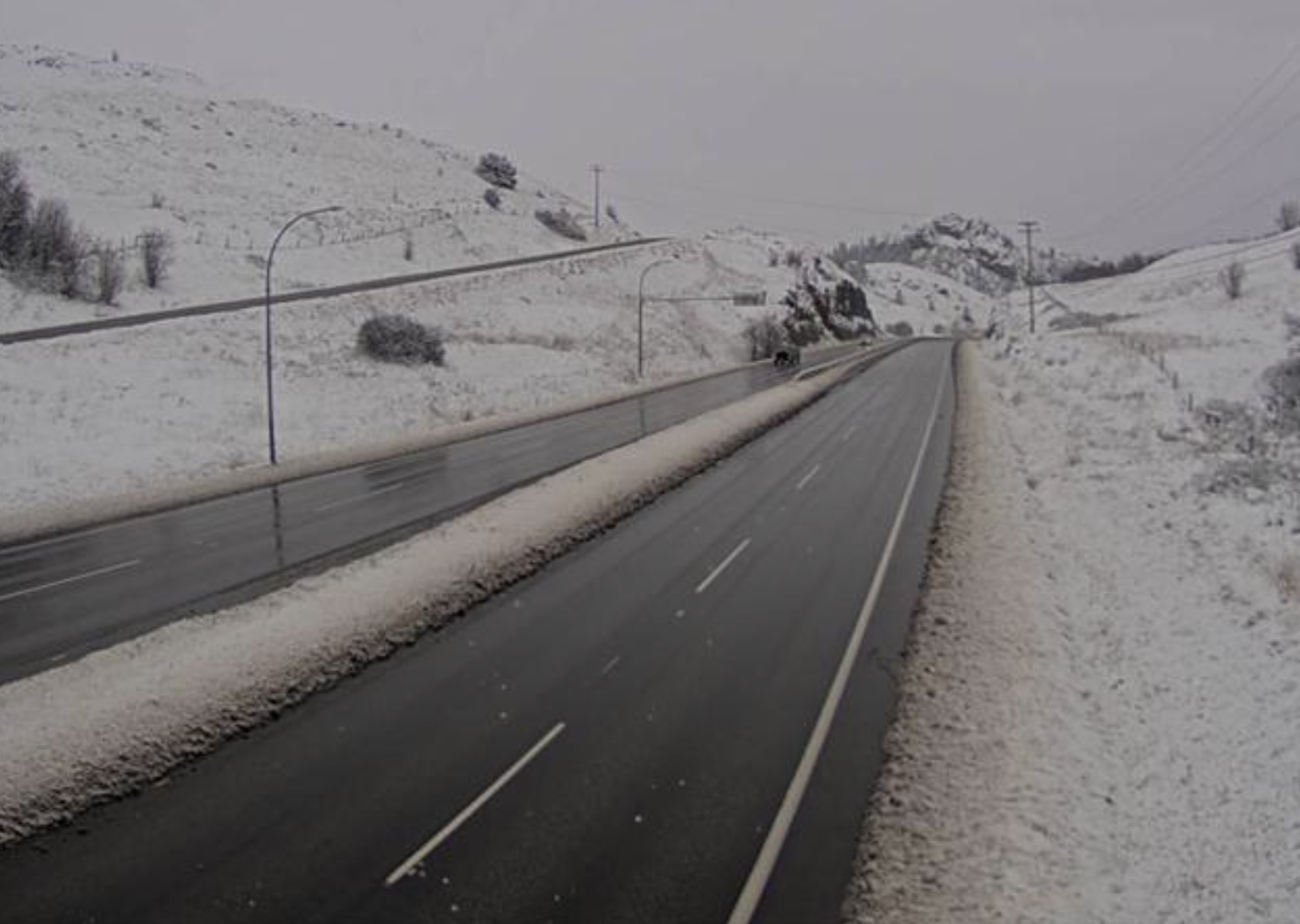 A wet highway with snow in the ditches and hills.