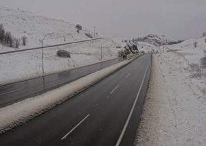 A wet highway with snow in the ditches and hills.