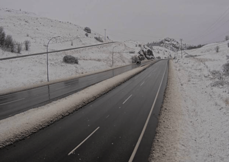 A wet highway with snow in the ditches and hills.