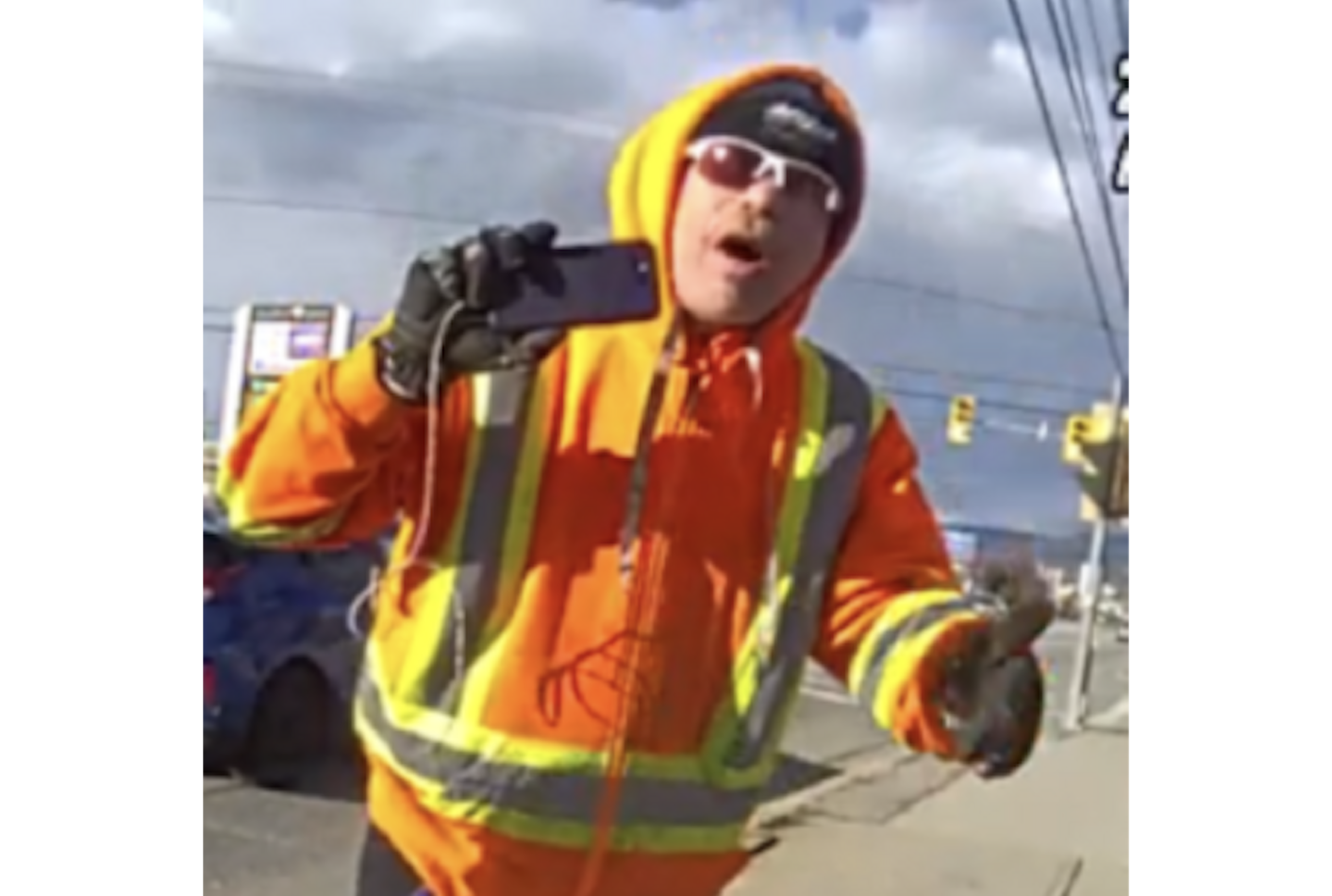 A man holding a phone in an orange jacket.