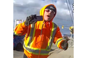 A man holding a phone in an orange jacket.
