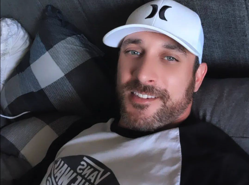 Christopher Muir wear a baseball cap and sits on a couch.