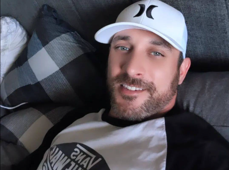 Christopher Muir wear a baseball cap and sits on a couch.