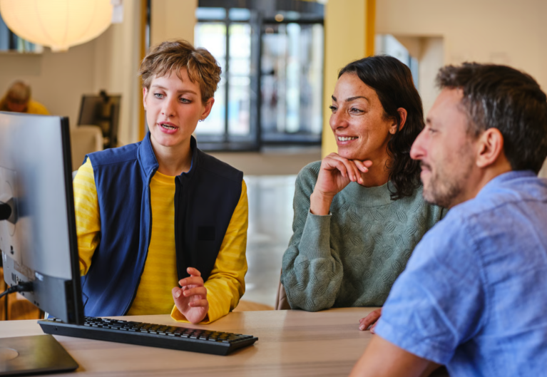 Three people smiling at a computer.