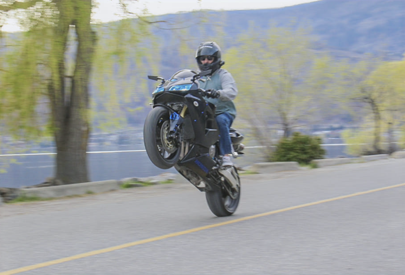 A motorcycle does a wheelie on a road by the lake.