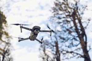 A drone flying with trees in the background.