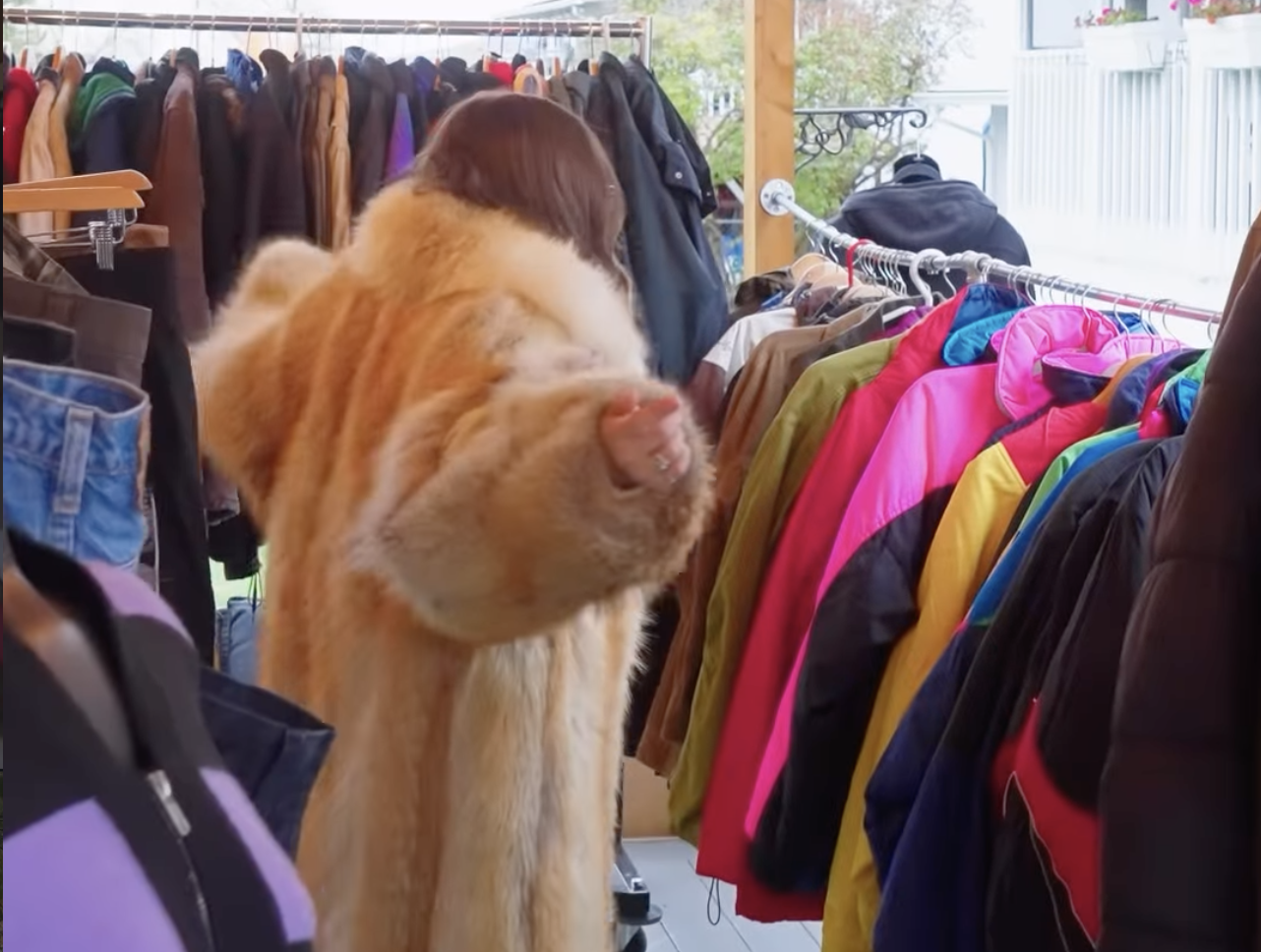 A person wearing a fur-like coat in a used clothing store.