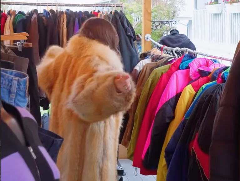 A person wearing a fur-like coat in a used clothing store.