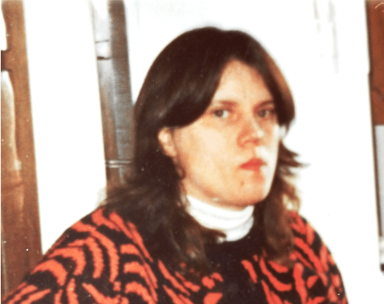 A woman wearing a red and black patterned sweater over a white turtle neck poses for a photo.