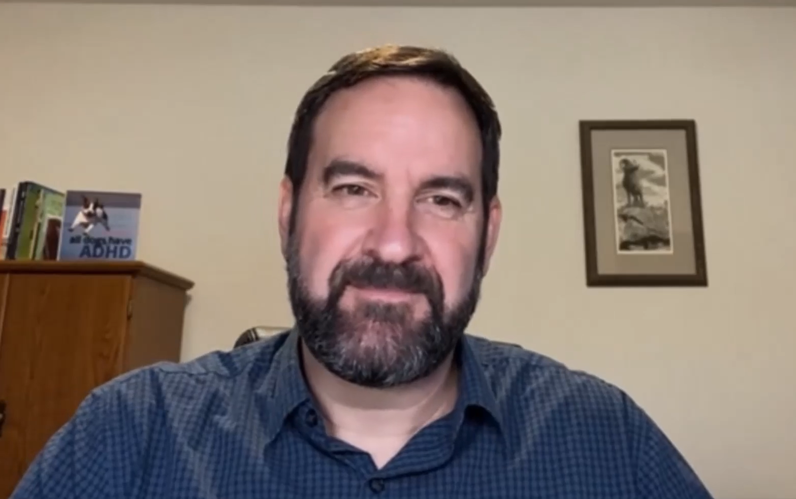 A man with a beard wears a blue shirt in a head and shoulders shot.
