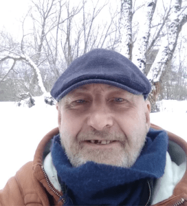 A man waering a flat cap and scarf in the snow.