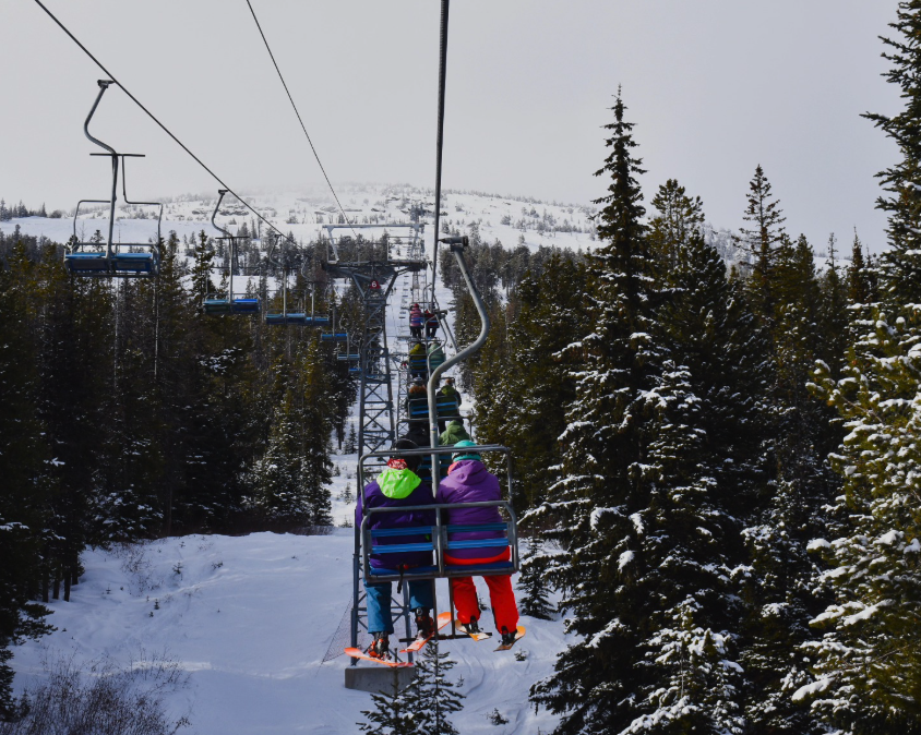 Two people sit on a ski lift, surrounded by tress.
