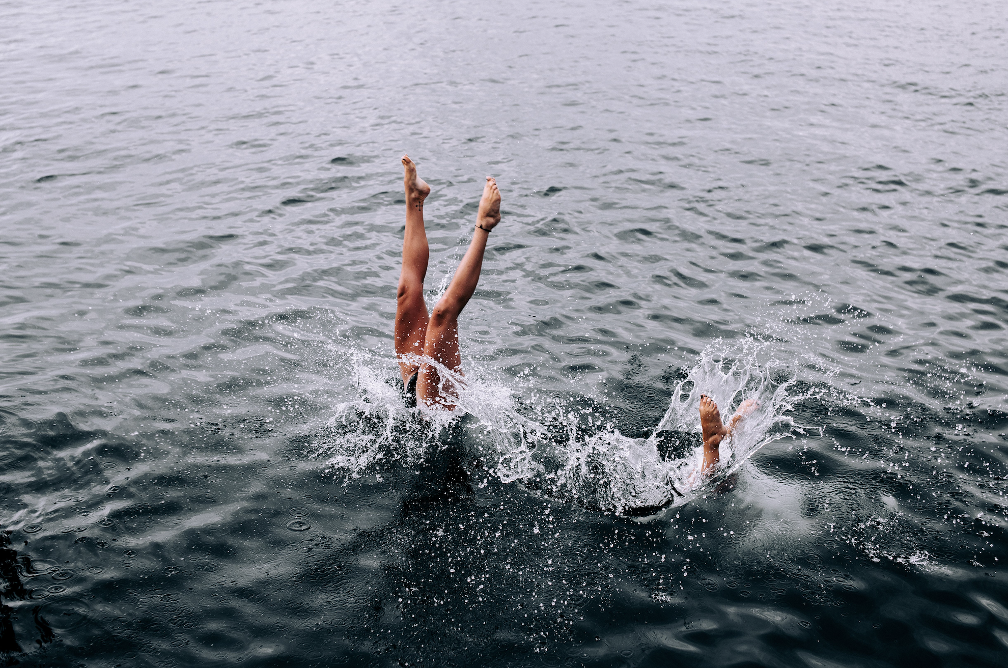 Two people diving into a lake. You can only see their legs.