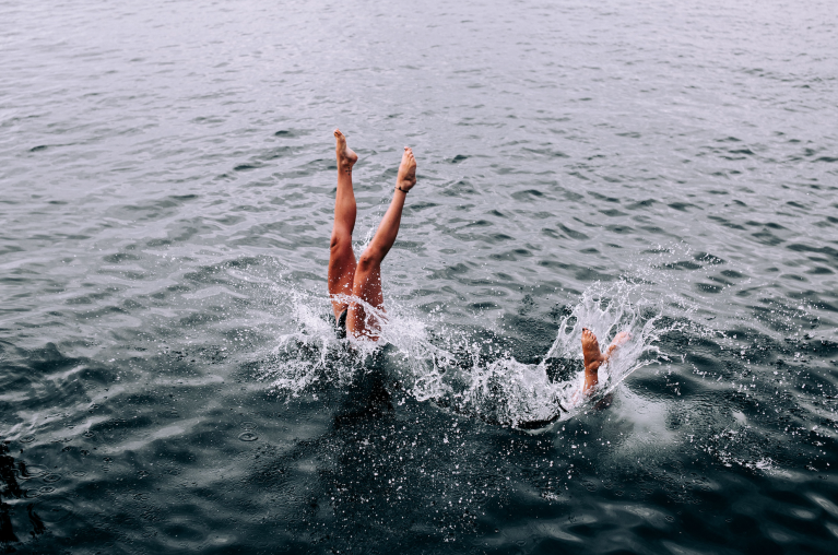 Two people diving into a lake. You can only see their legs.