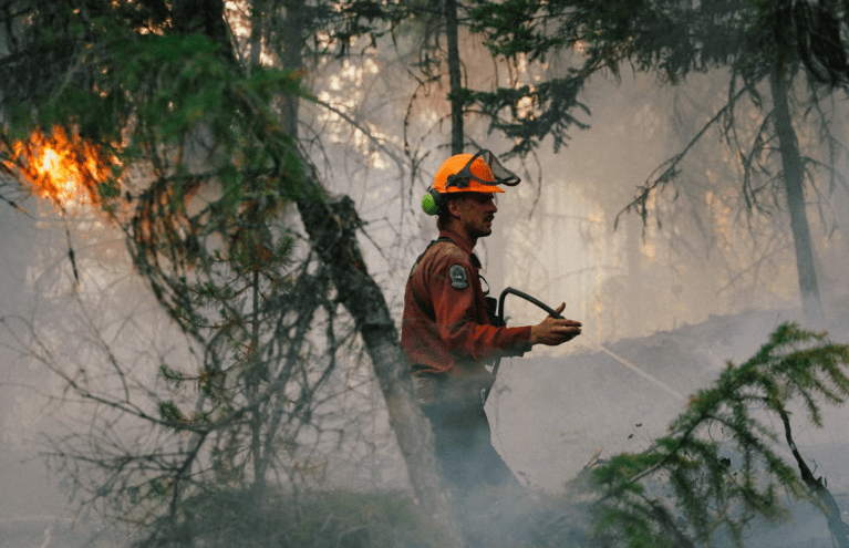 A BC Wildfire Service worker sprays a hose in a burning forest.