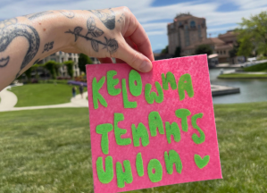 A person holding a sign for the Kelowna Tenants Union.