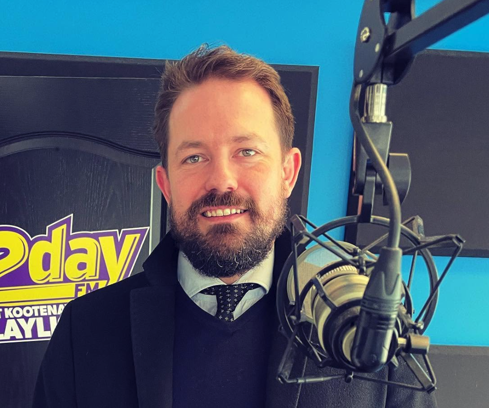 A man with a beard stands in front of a microphone.