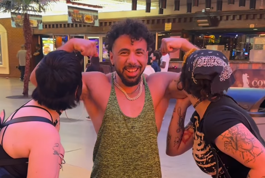 Two woman kiss the arms of a man wearing a vest.
