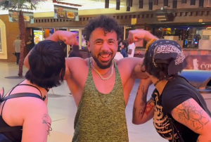 Two woman kiss the arms of a man wearing a vest.