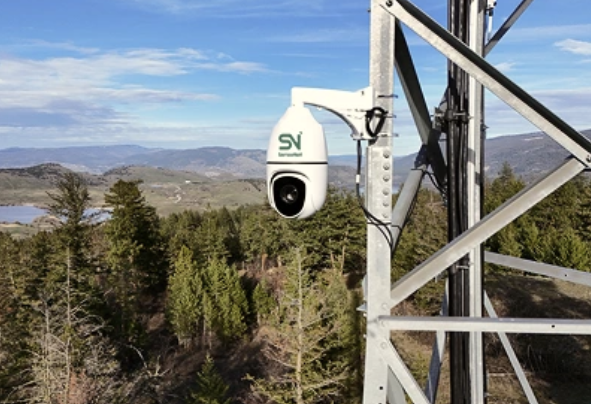 A high tech camera on a pole with a forest in the background.