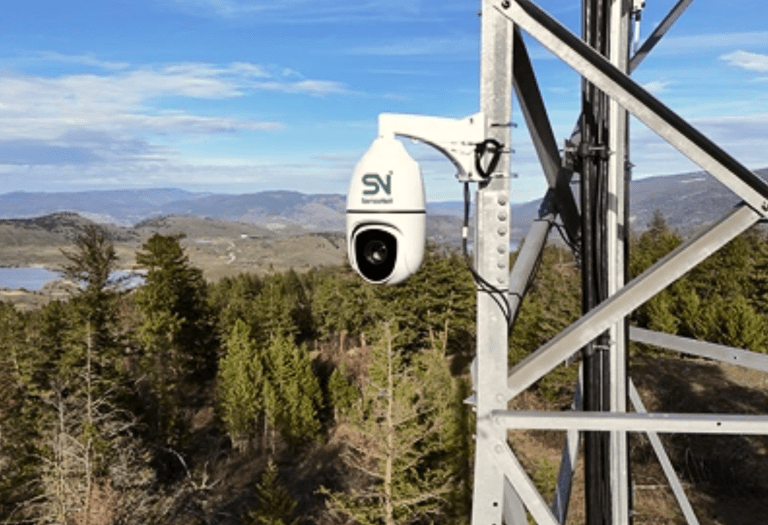 A high tech camera on a pole with a forest in the background.