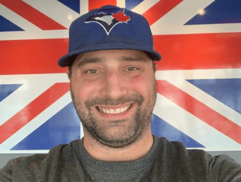 A man wearing a Blue Jays cap poses for a photo in front of the Union Jack.