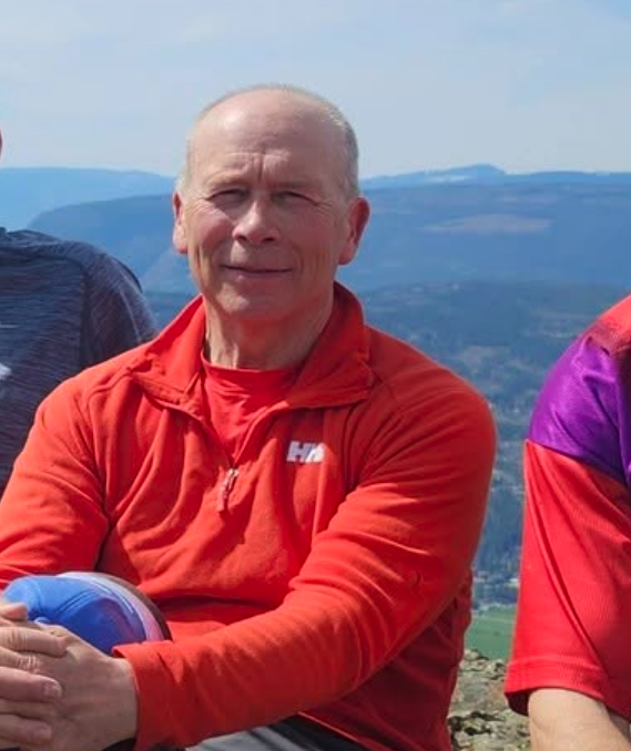 A bald man in a red with mountains in the background.