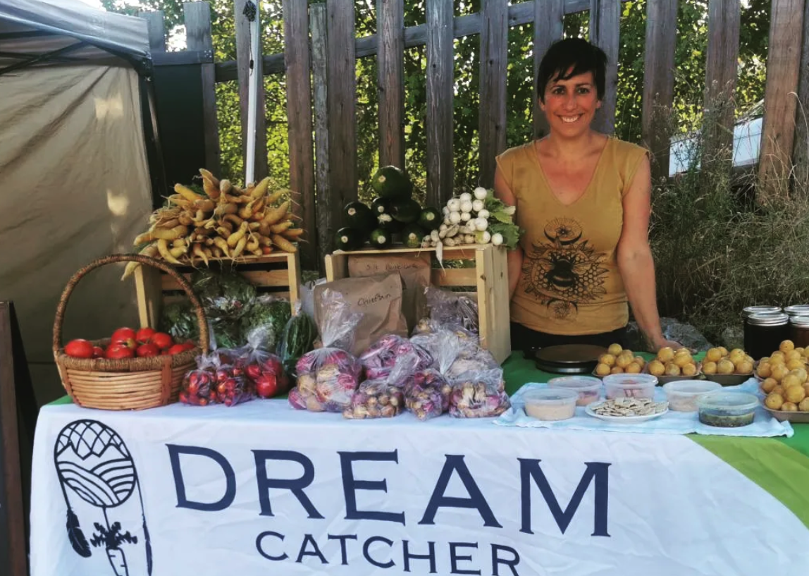 A woman stands behind a farm stall selling vegetables.