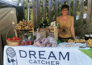 A woman stands behind a farm stall selling vegetables.