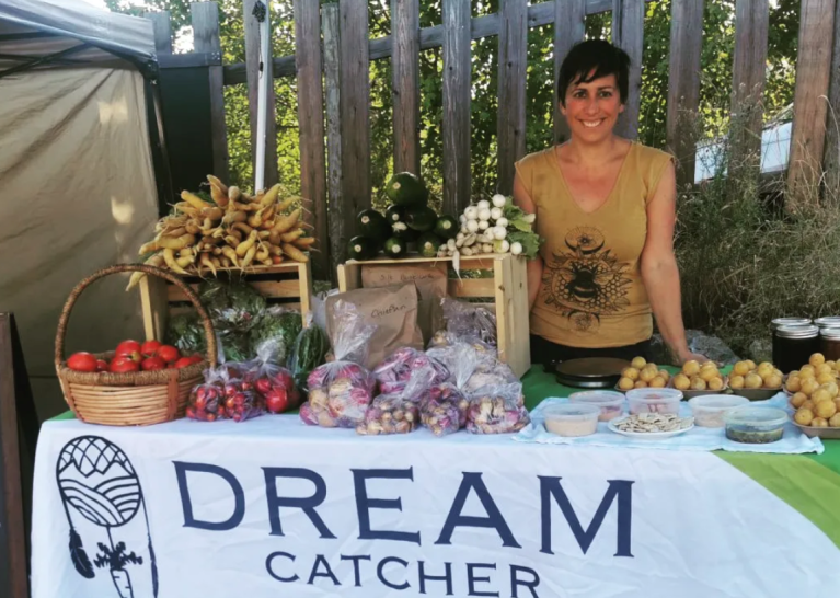 A woman stands behind a farm stall selling vegetables.