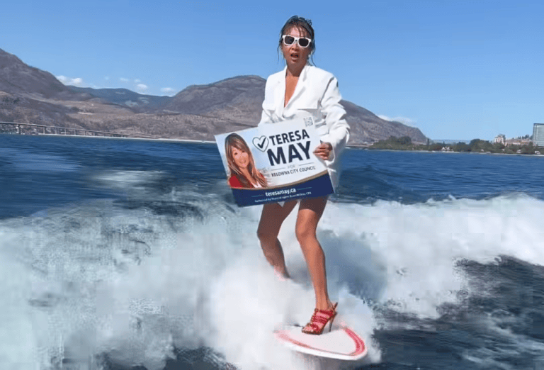 A woman in a white business jacket wake boarding while holding an election campaign sign.