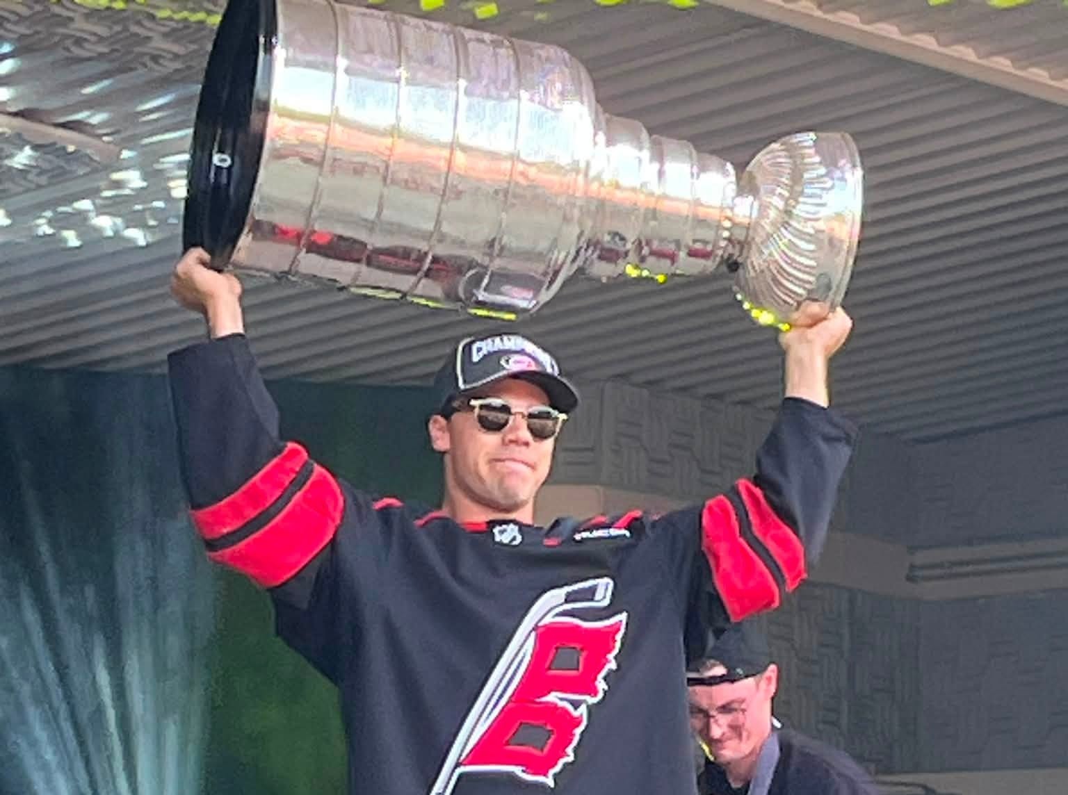 A man in a hockey jersey holds the Stanley Cup over his head.