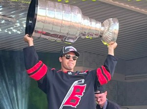 A man in a hockey jersey holds the Stanley Cup over his head.