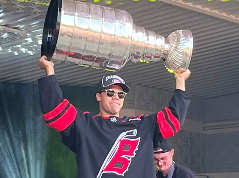 A man in a hockey jersey holds the Stanley Cup over his head.