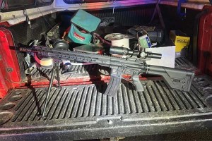 A carbine rifle with a scope on the tail gate of a truck.