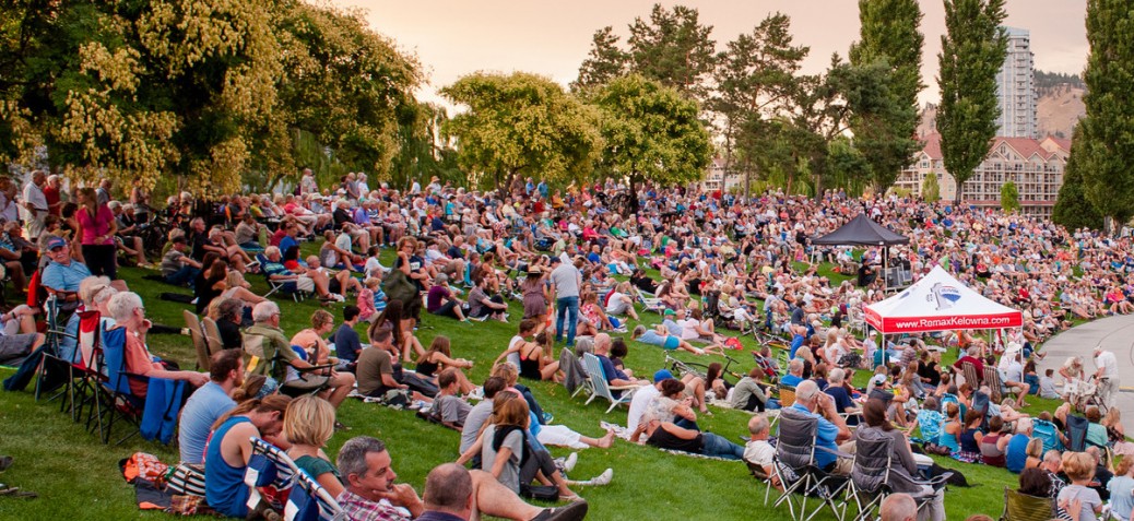 A large quantity of people sitting on the grass watching a presentation