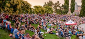 A large quantity of people sitting on the grass watching a presentation