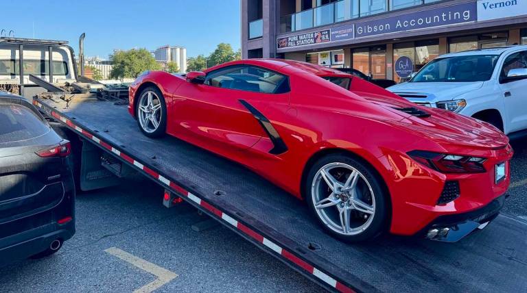 A red 2025 Corvette is being loaded onto a tow truck.