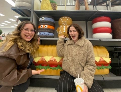 Two young women pose in front of thrift store shelf.