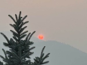 Sun rising over a mountain is orange through wildfire smoke.
