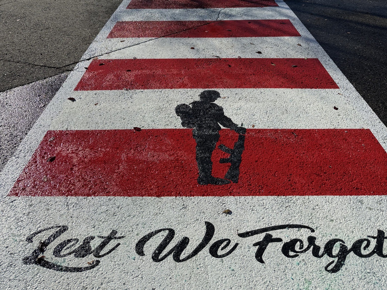 A red and white crosswalk has a soldier and the words Lest We Forget painted on it.